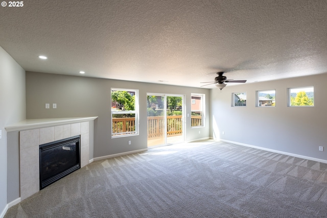unfurnished living room with a tile fireplace, carpet floors, ceiling fan, baseboards, and a textured ceiling