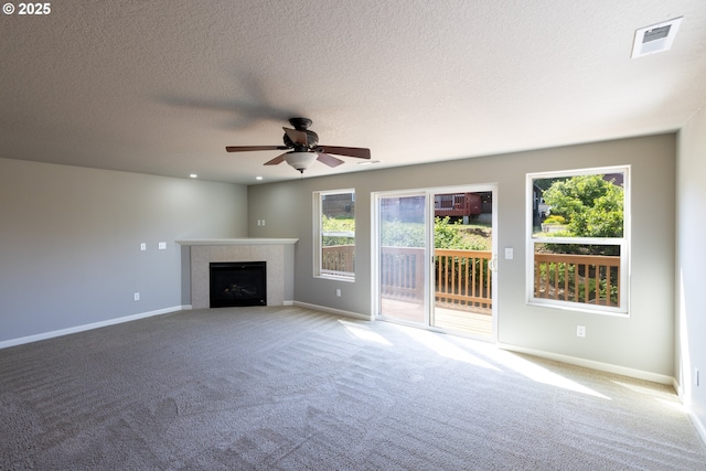 unfurnished living room featuring carpet, healthy amount of natural light, ceiling fan, a tile fireplace, and a textured ceiling