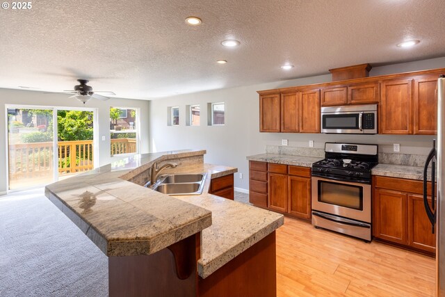 kitchen featuring appliances with stainless steel finishes, a sink, a textured ceiling, brown cabinetry, and recessed lighting
