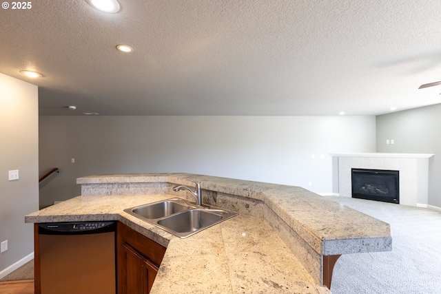 kitchen with dishwasher, a sink, a textured ceiling, recessed lighting, and a fireplace