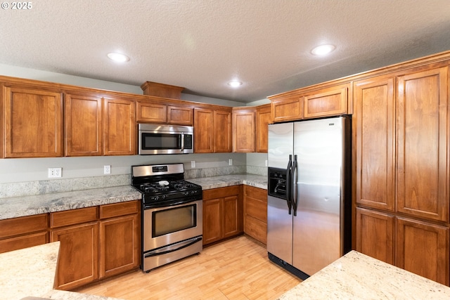 kitchen with stainless steel appliances, brown cabinetry, light wood-style flooring, a textured ceiling, and recessed lighting