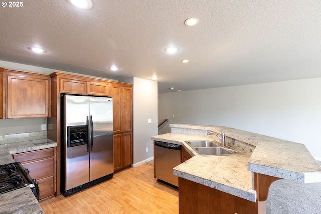 kitchen featuring stainless steel appliances, a sink, light countertops, light wood finished floors, and a textured ceiling