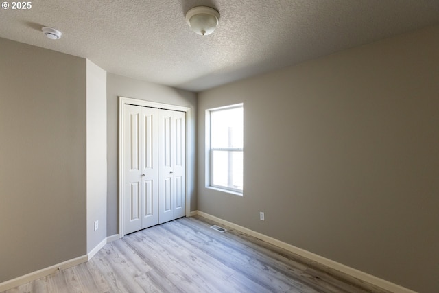 unfurnished bedroom featuring light wood-style flooring, a closet, baseboards, and a textured ceiling