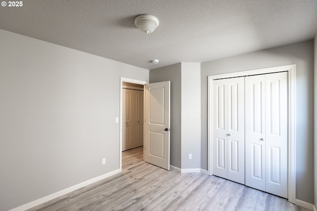 unfurnished bedroom featuring light wood-style floors, baseboards, a closet, and a textured ceiling