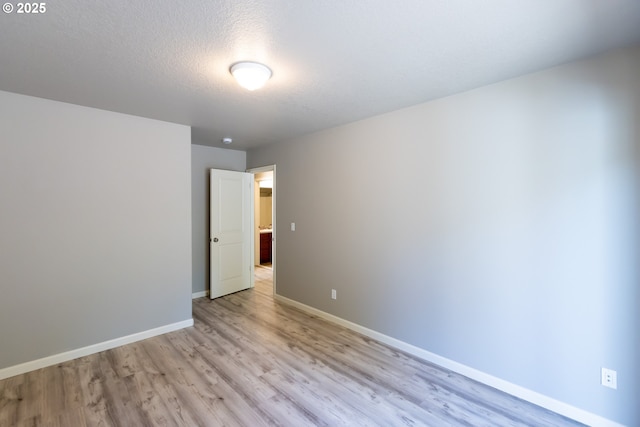 spare room with light wood-style floors, baseboards, and a textured ceiling