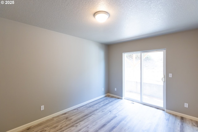 empty room featuring light wood-type flooring, a textured ceiling, and baseboards