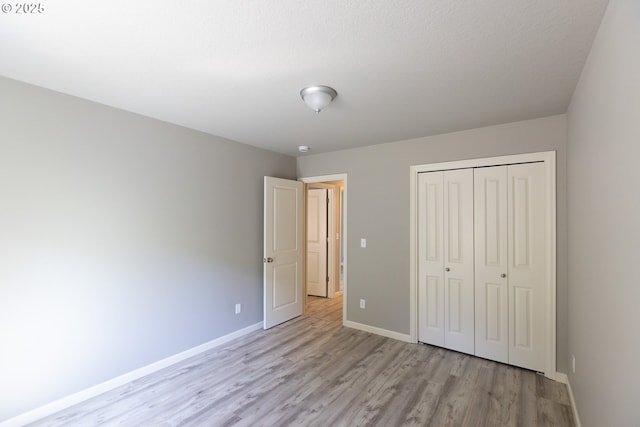 unfurnished bedroom featuring light wood-style flooring, baseboards, and a closet