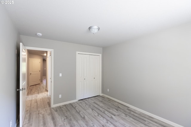unfurnished bedroom with light wood finished floors, baseboards, and a closet