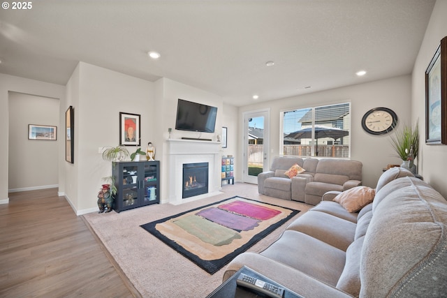 living room featuring a fireplace with flush hearth, recessed lighting, baseboards, and wood finished floors