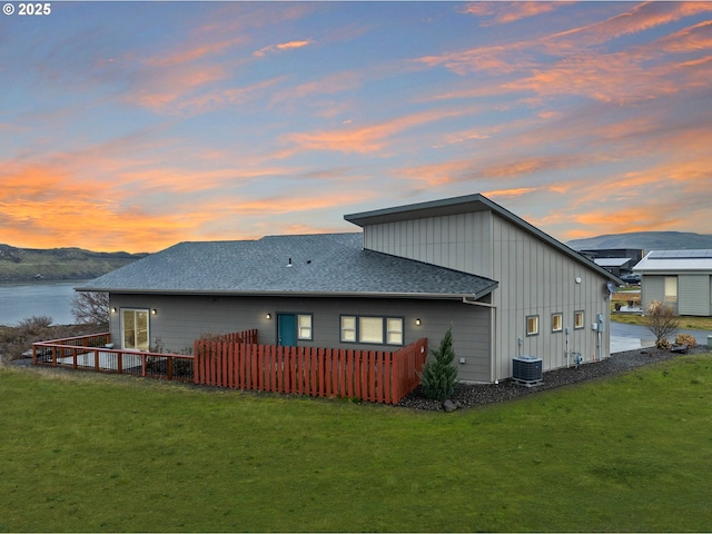 back of property with roof with shingles, a yard, a water view, board and batten siding, and central AC