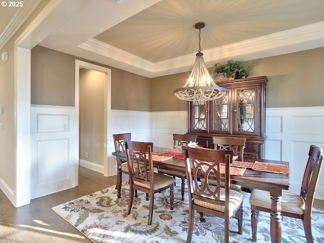 dining room featuring wood finished floors, a tray ceiling, crown molding, a decorative wall, and a notable chandelier