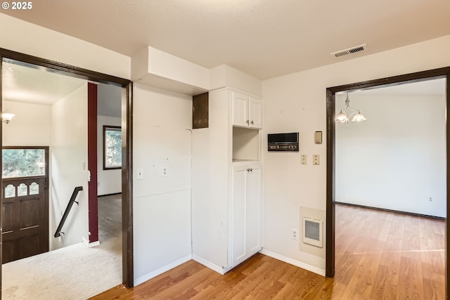 spare room with light wood-style flooring, visible vents, a chandelier, and baseboards