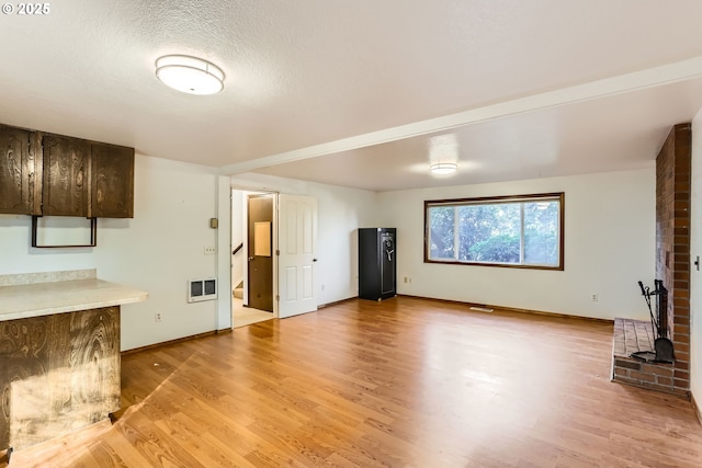 unfurnished living room featuring light wood-style floors, visible vents, a textured ceiling, and baseboards