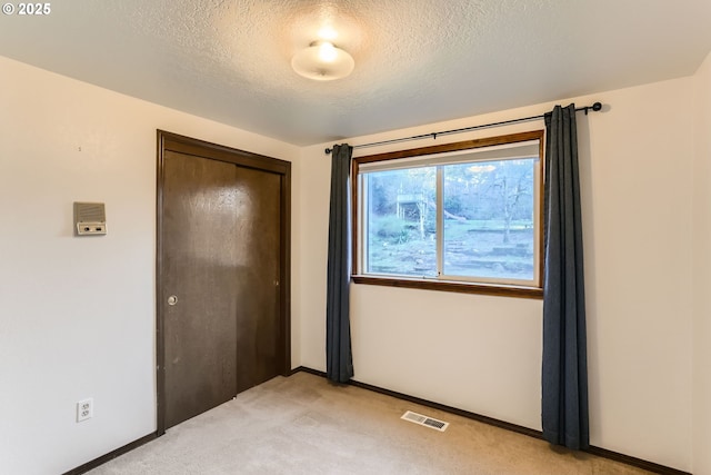 unfurnished bedroom featuring a textured ceiling, light carpet, visible vents, baseboards, and a closet