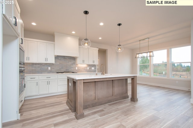 kitchen featuring appliances with stainless steel finishes, premium range hood, white cabinetry, pendant lighting, and a center island with sink