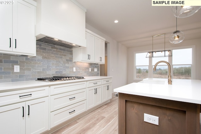 kitchen featuring white cabinetry, sink, hanging light fixtures, premium range hood, and stainless steel gas stovetop