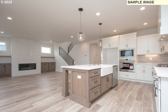 kitchen featuring pendant lighting, white cabinetry, appliances with stainless steel finishes, and an island with sink