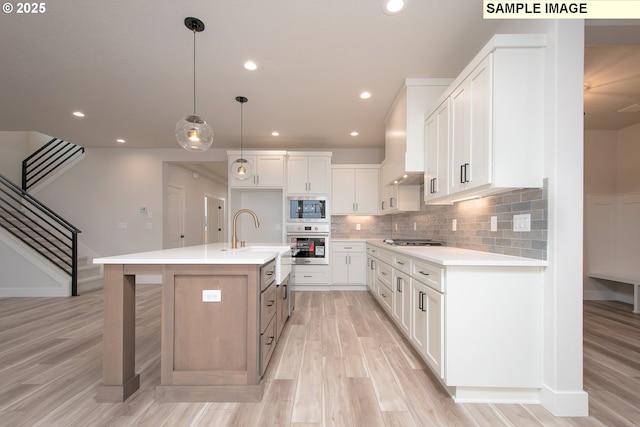 kitchen with pendant lighting, appliances with stainless steel finishes, sink, white cabinetry, and an island with sink