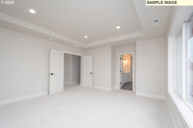 unfurnished bedroom featuring light colored carpet, a tray ceiling, and ensuite bathroom