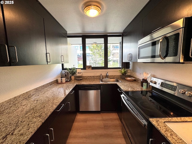 kitchen with a sink, a textured ceiling, appliances with stainless steel finishes, and dark cabinetry