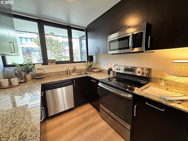 kitchen featuring light wood-style flooring, appliances with stainless steel finishes, dark cabinetry, a textured ceiling, and a sink