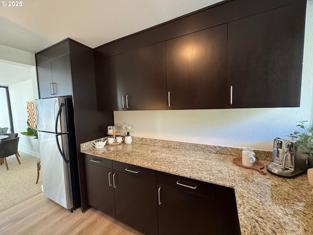 kitchen featuring light stone countertops, light wood-style floors, and freestanding refrigerator