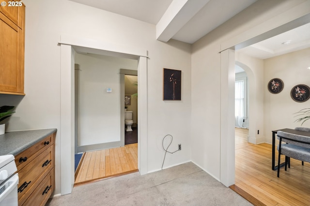 hallway with baseboards, arched walkways, and light wood finished floors