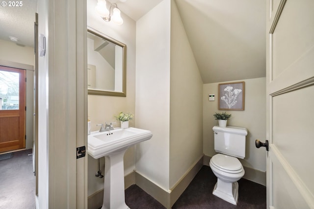 bathroom featuring a sink, baseboards, toilet, and vaulted ceiling