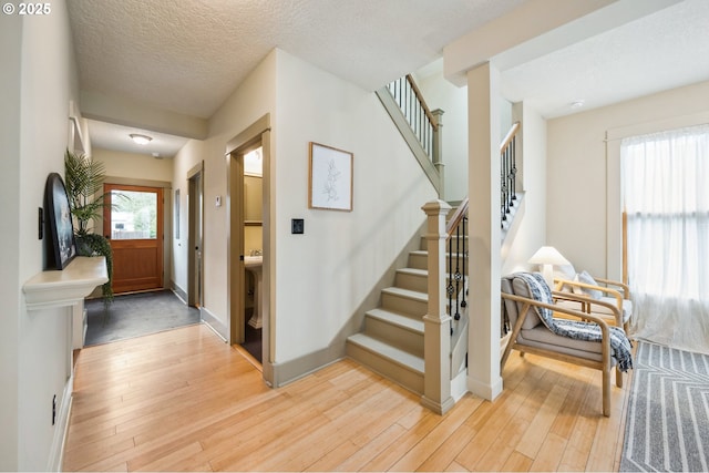 foyer entrance with light wood finished floors, a textured ceiling, stairs, and baseboards