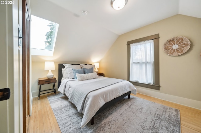 bedroom with baseboards, lofted ceiling with skylight, and wood finished floors