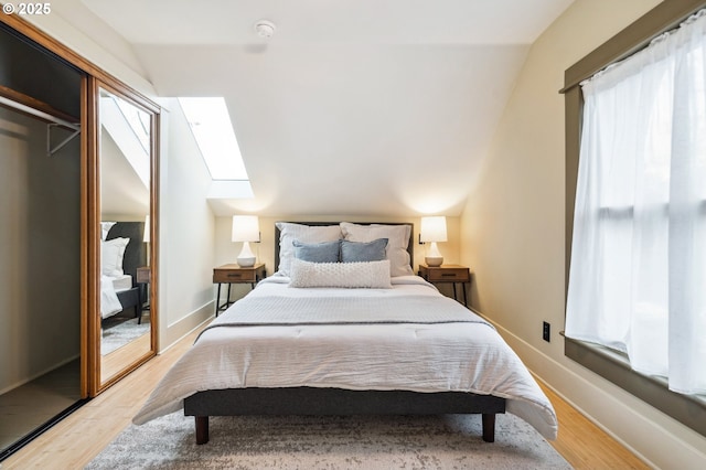 bedroom featuring light wood-type flooring, vaulted ceiling with skylight, baseboards, and a closet