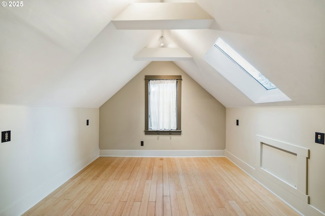 additional living space featuring baseboards, lofted ceiling with skylight, and wood finished floors