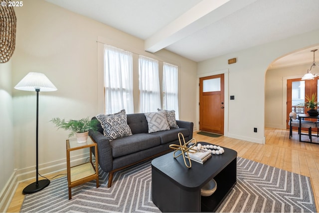 living area with hardwood / wood-style floors, baseboards, arched walkways, beamed ceiling, and a notable chandelier