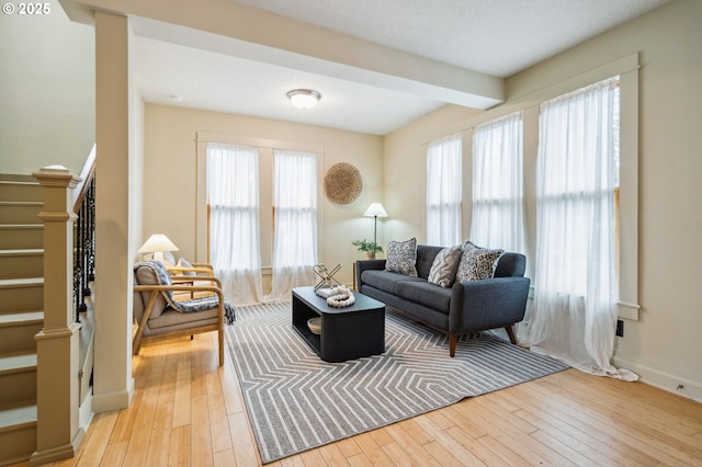 living room with light wood-type flooring, baseboards, beamed ceiling, and stairs