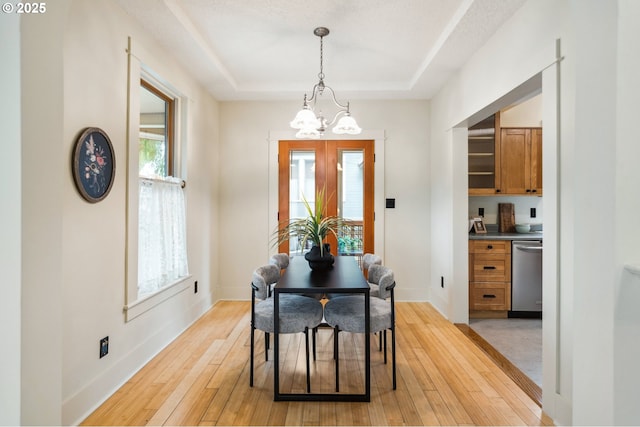 dining room with a tray ceiling, light wood-style floors, baseboards, and a chandelier