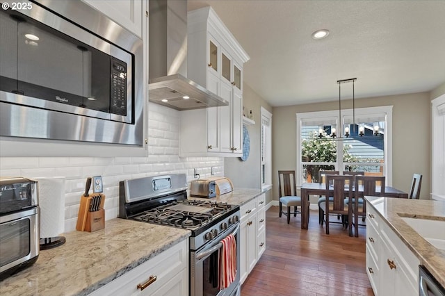 2871 Wing Tip Ave, Salem, OR 97304 - kitchen featuring appliances with stainless steel finishes, wall chimney range hood, decorative backsplash, white cabinetry, and hanging light fixtures
