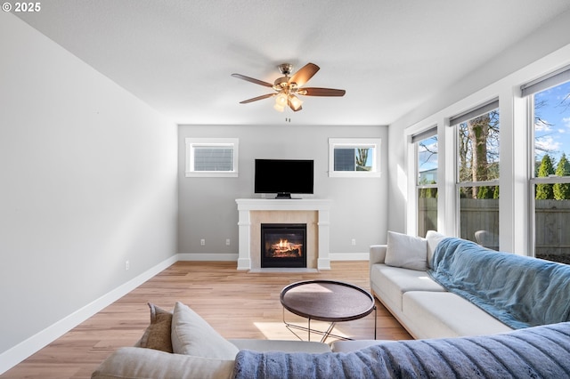 living room featuring light wood-style flooring, baseboards, ceiling fan, and a fireplace with flush hearth