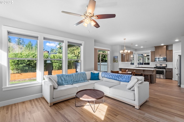 living area with light wood finished floors, ceiling fan with notable chandelier, baseboards, and recessed lighting