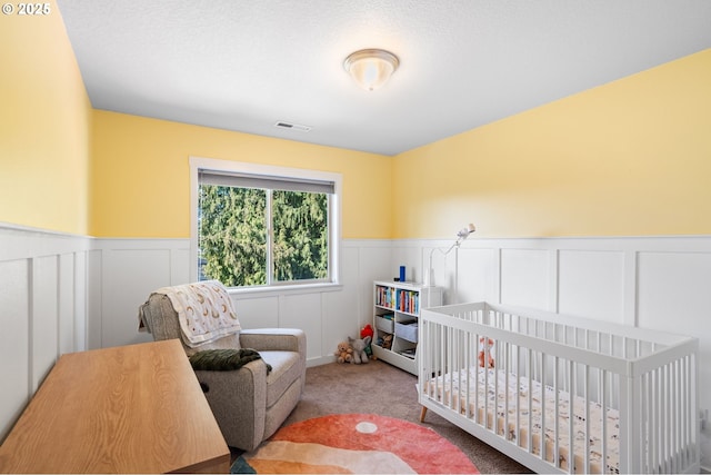 bedroom with carpet floors, a crib, visible vents, and wainscoting