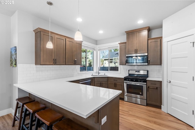 kitchen featuring a breakfast bar area, a peninsula, a sink, appliances with stainless steel finishes, and light wood-type flooring