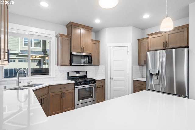 kitchen with tasteful backsplash, stainless steel appliances, light countertops, pendant lighting, and a sink