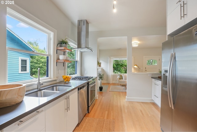 kitchen with appliances with stainless steel finishes, island exhaust hood, a sink, light wood-style floors, and white cabinets