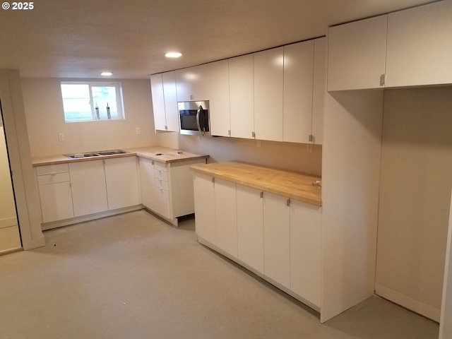 kitchen featuring stainless steel microwave, recessed lighting, white cabinetry, and concrete flooring