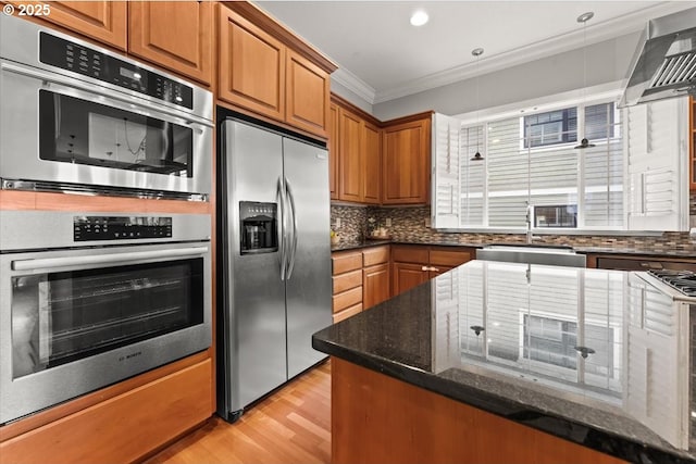 kitchen with sink, crown molding, stainless steel fridge, wall chimney range hood, and dark stone counters