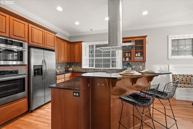 kitchen featuring crown molding, island exhaust hood, stainless steel appliances, and a kitchen bar