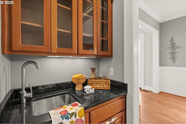 kitchen with dark stone countertops, sink, crown molding, and light hardwood / wood-style flooring