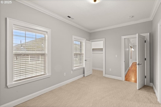 unfurnished bedroom with a walk in closet, ornamental molding, a closet, and light carpet