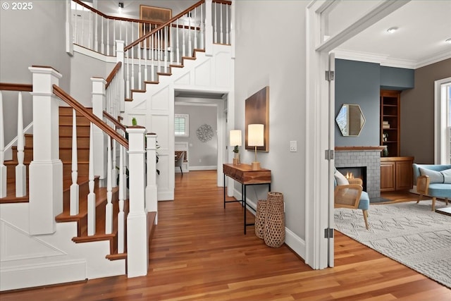 foyer entrance with a tiled fireplace, crown molding, a towering ceiling, and hardwood / wood-style flooring