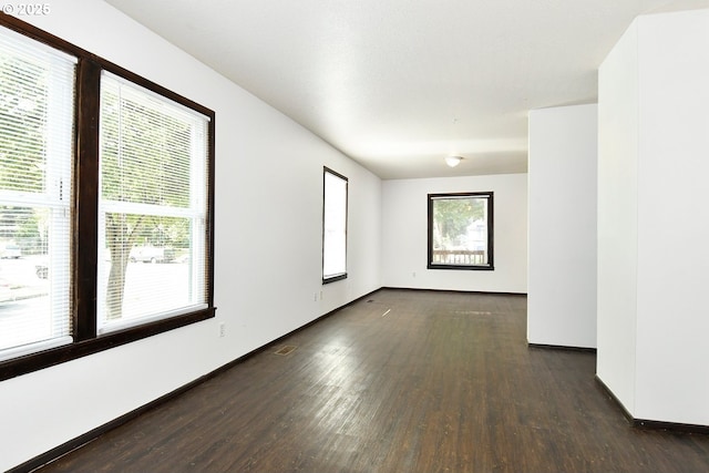 empty room featuring visible vents, baseboards, a healthy amount of sunlight, and wood finished floors