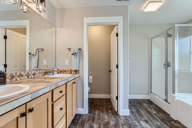 bathroom featuring toilet, wood-type flooring, vanity, backsplash, and a shower with door